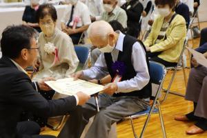 百寿を迎えた方へ記念品を手渡す様子